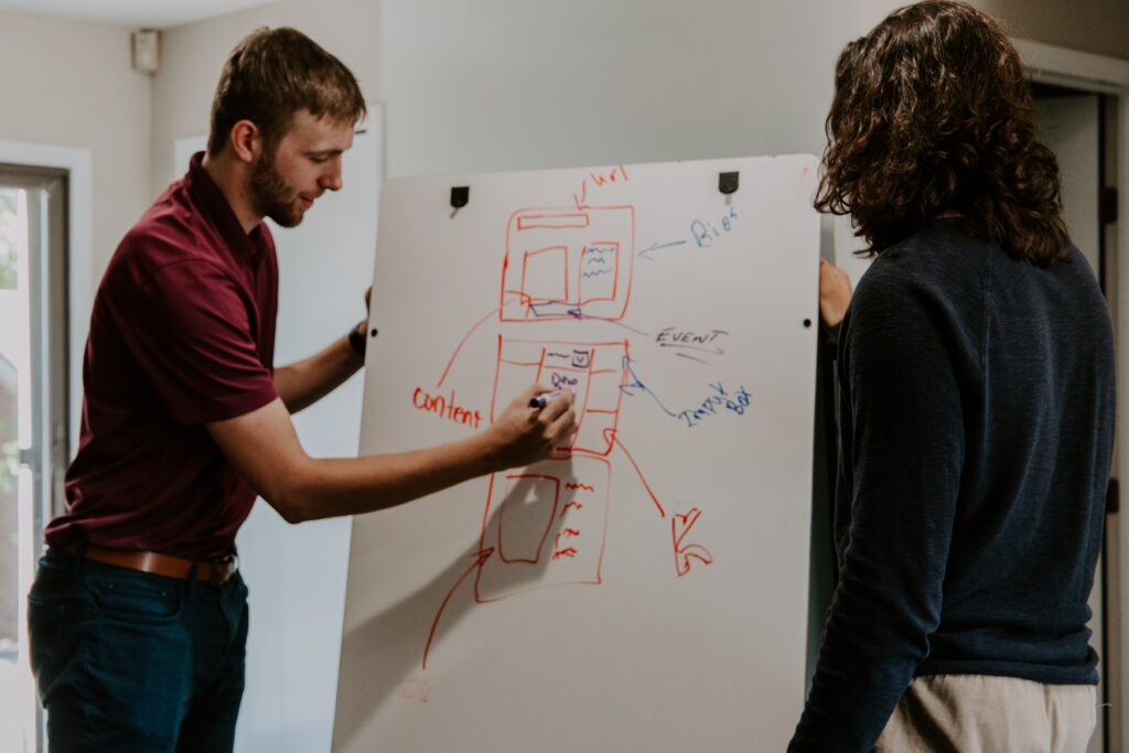 white male writing on a whiteboard with a woman watching him